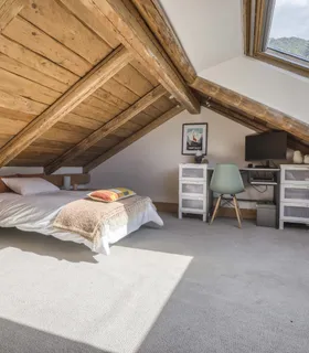 Lit simple sous plafond mansardé dans un décor alpin Appartement à louer à Chamonix – coin nuit en mezzanine avec lit simple dans le Prakka High Camp, décoré en bois avec lumière naturelle à Les Houches.